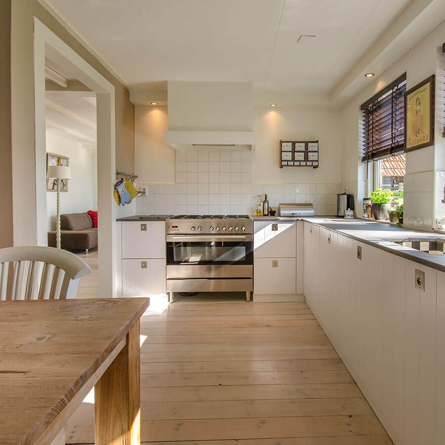 Kitchen with white cabinets, light wood floor, stainless steel oven, and window with blinds.