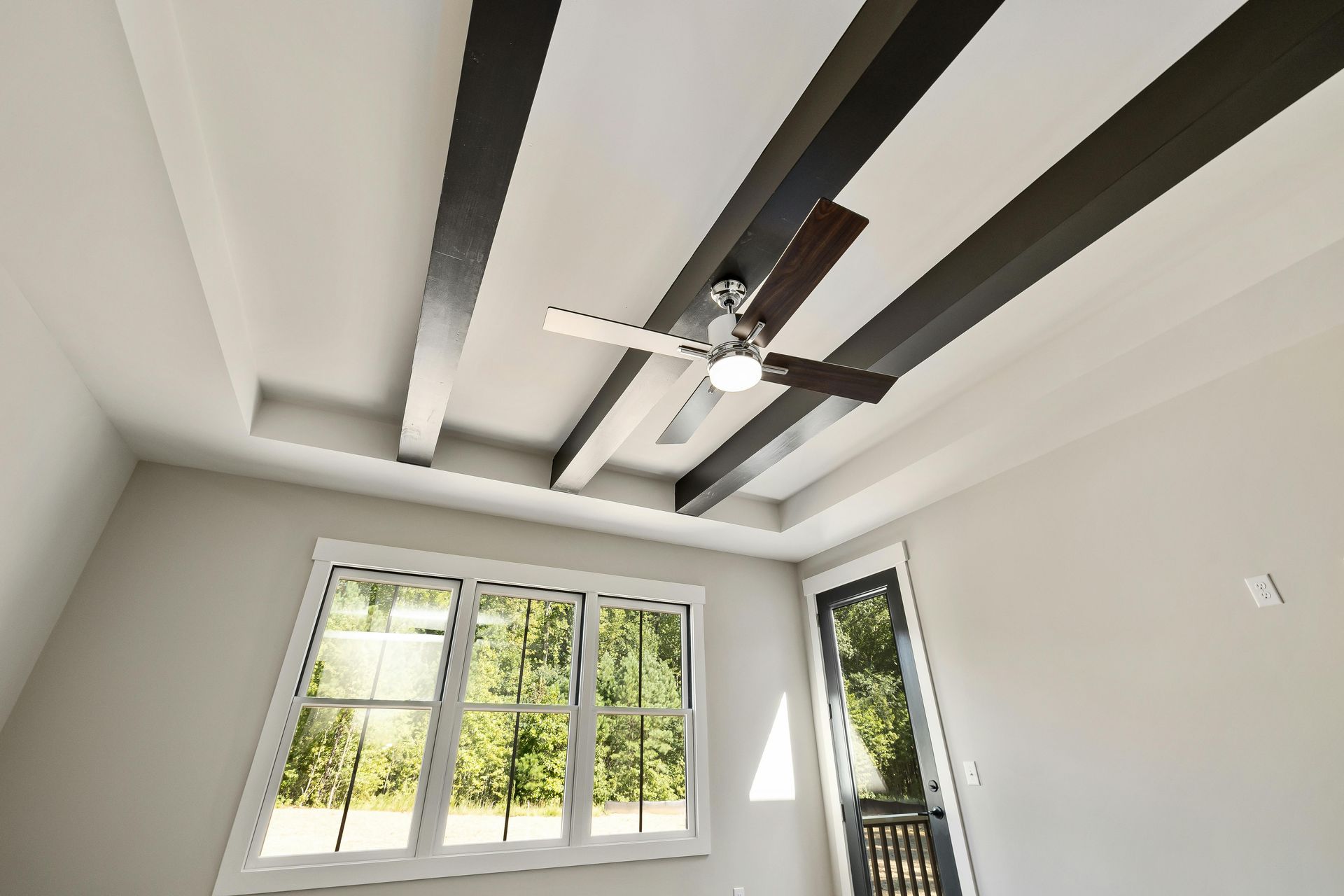Room interior with white walls, window, dark ceiling beams, and a ceiling fan.