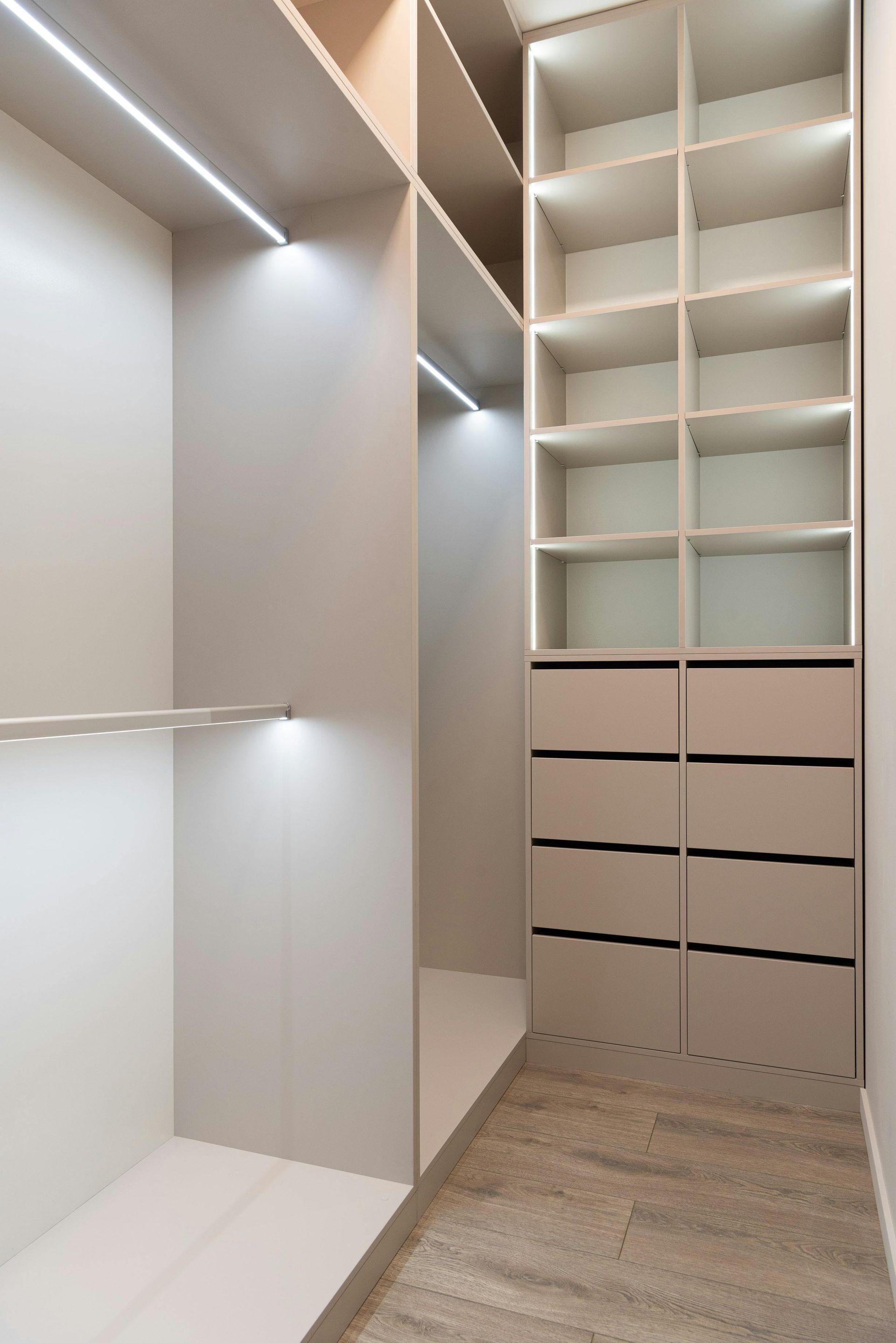 Walk-in closet with beige built-in shelves, drawers, and LED lighting.