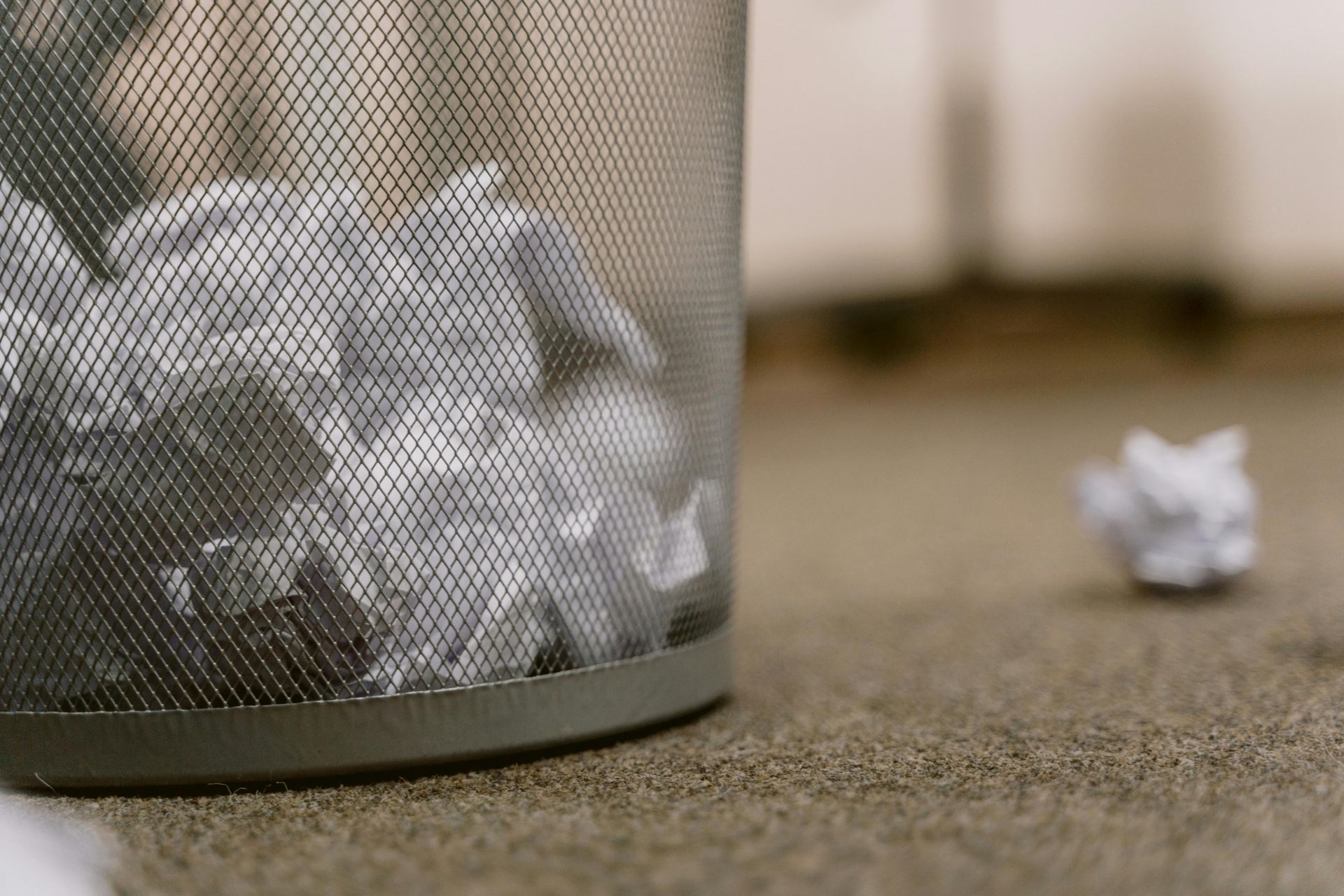 Trash can overflowing with crumpled paper; one paper ball on the carpet.