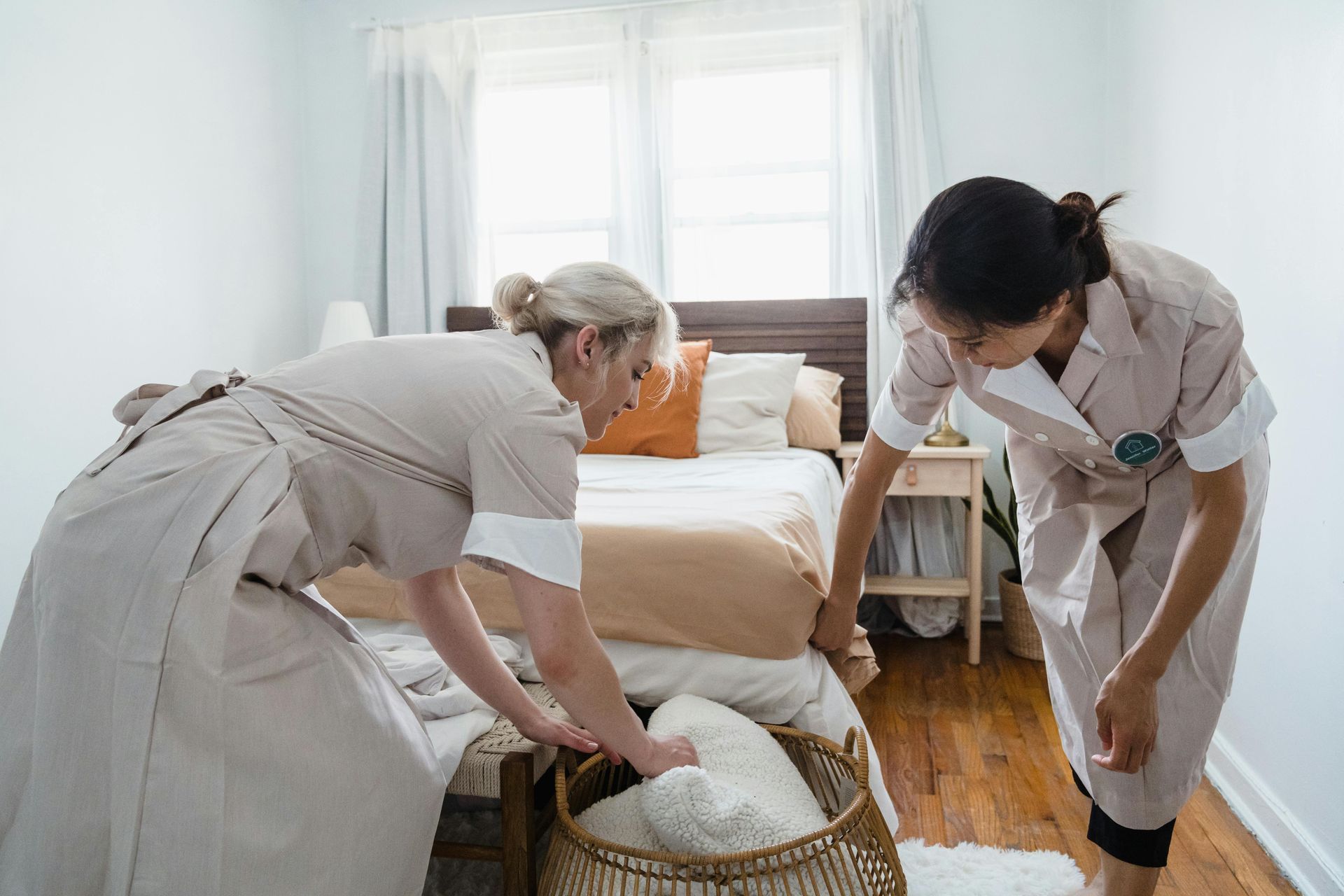 Two people in uniform making a bed in a bedroom.