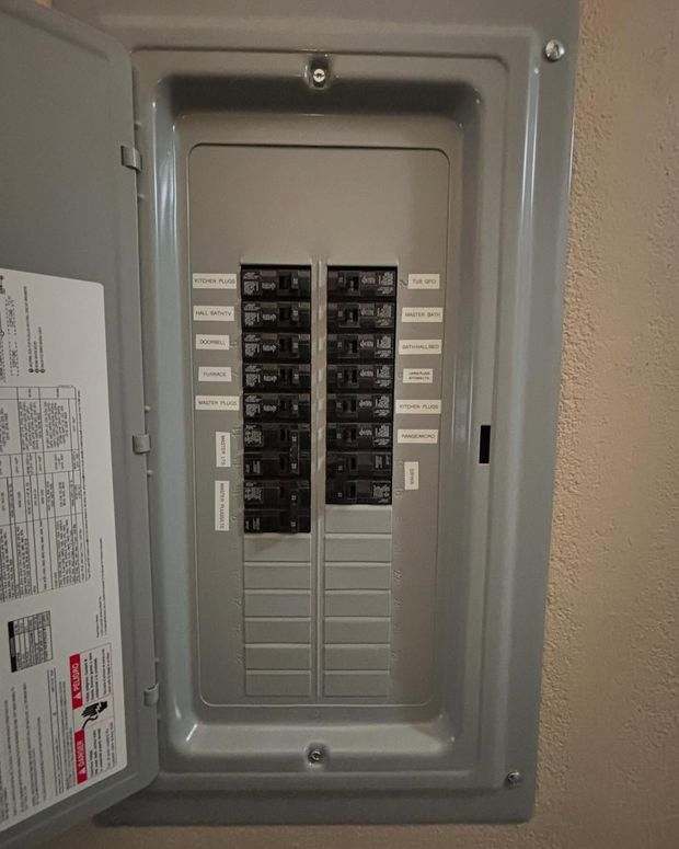 Open gray electrical panel with circuit breakers and labels.