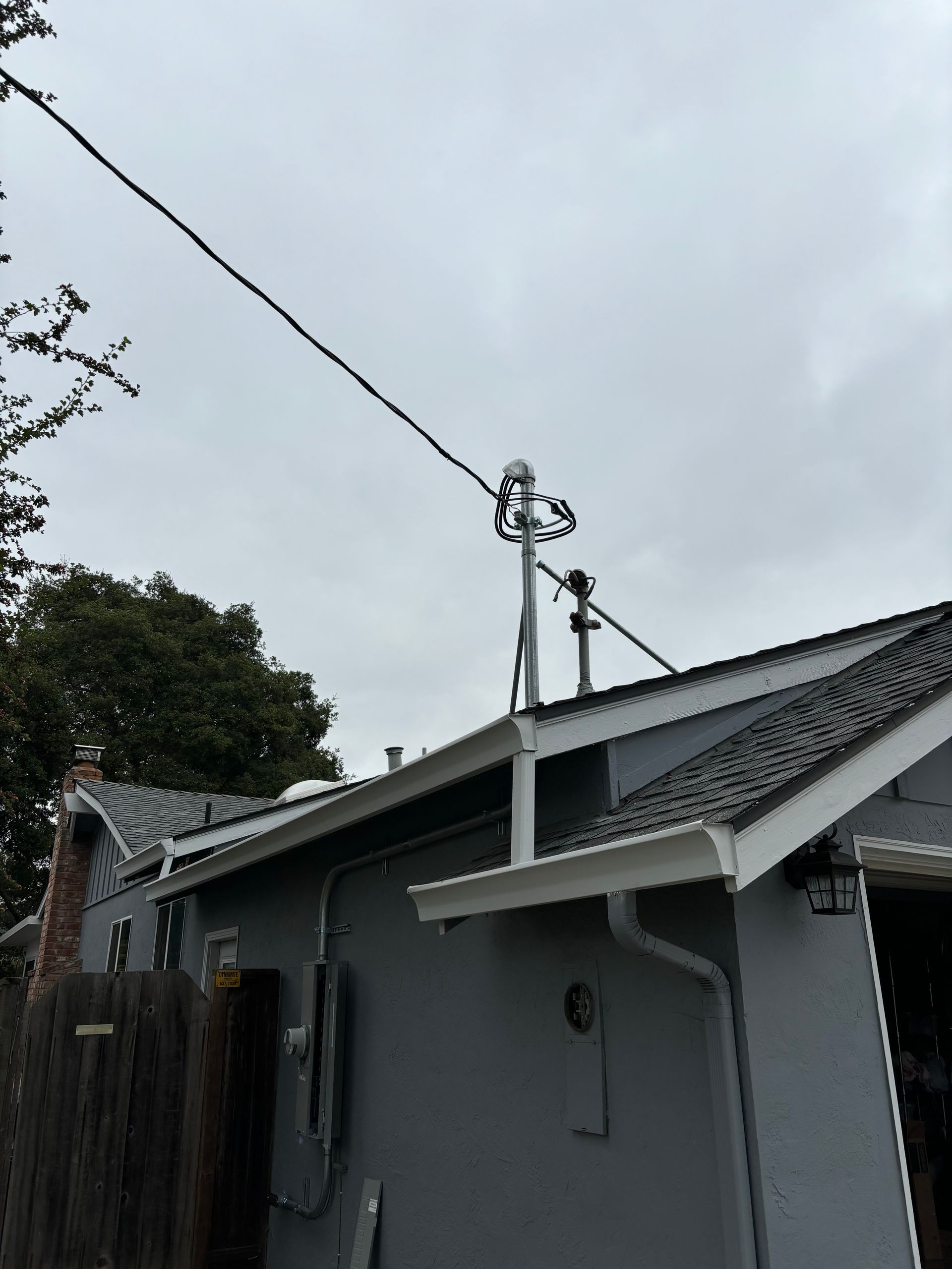 Gray house with a pole on the roof holding electrical equipment, including insulators and wires, connected to a power line.