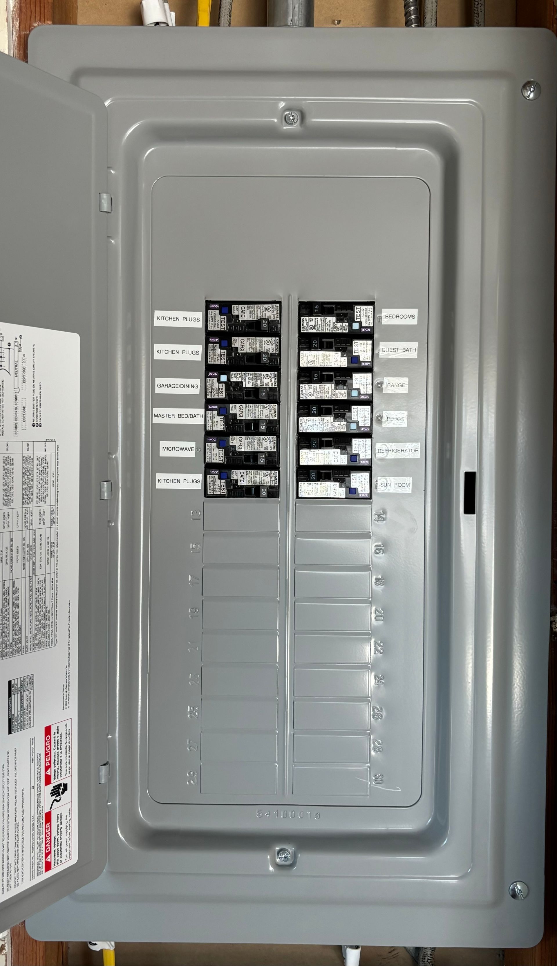 Opened electrical panel with labeled circuit breakers in a gray metal box.