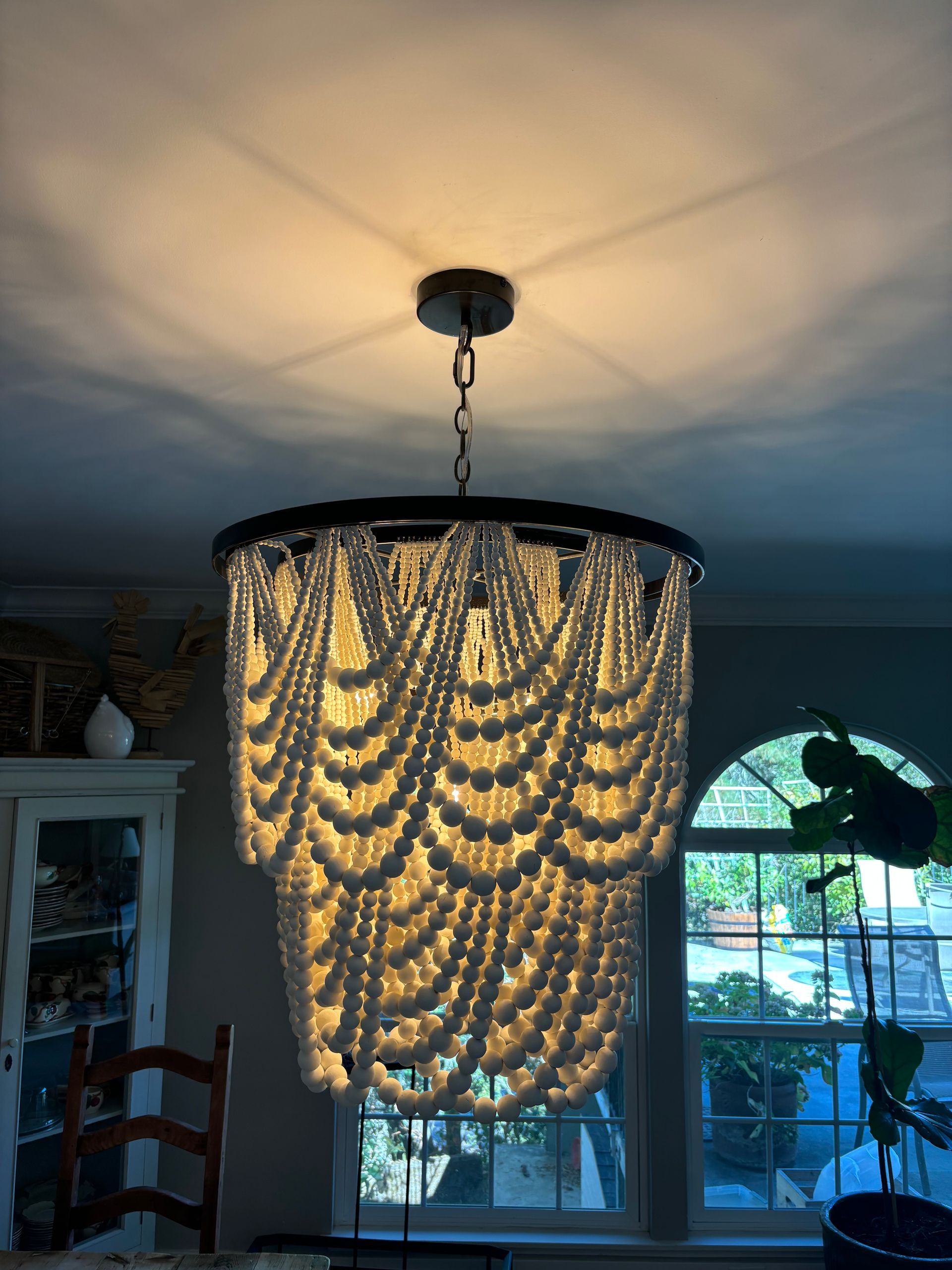 Chandelier with cascading white beads, hanging from a ceiling. Window and cabinet visible in background.