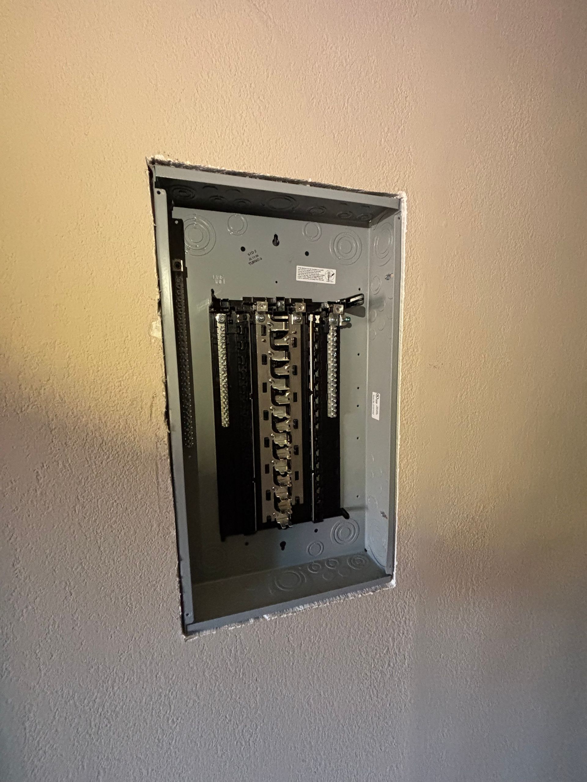 Electrical breaker panel recessed in a wall. Gray metal box with black circuit breakers.