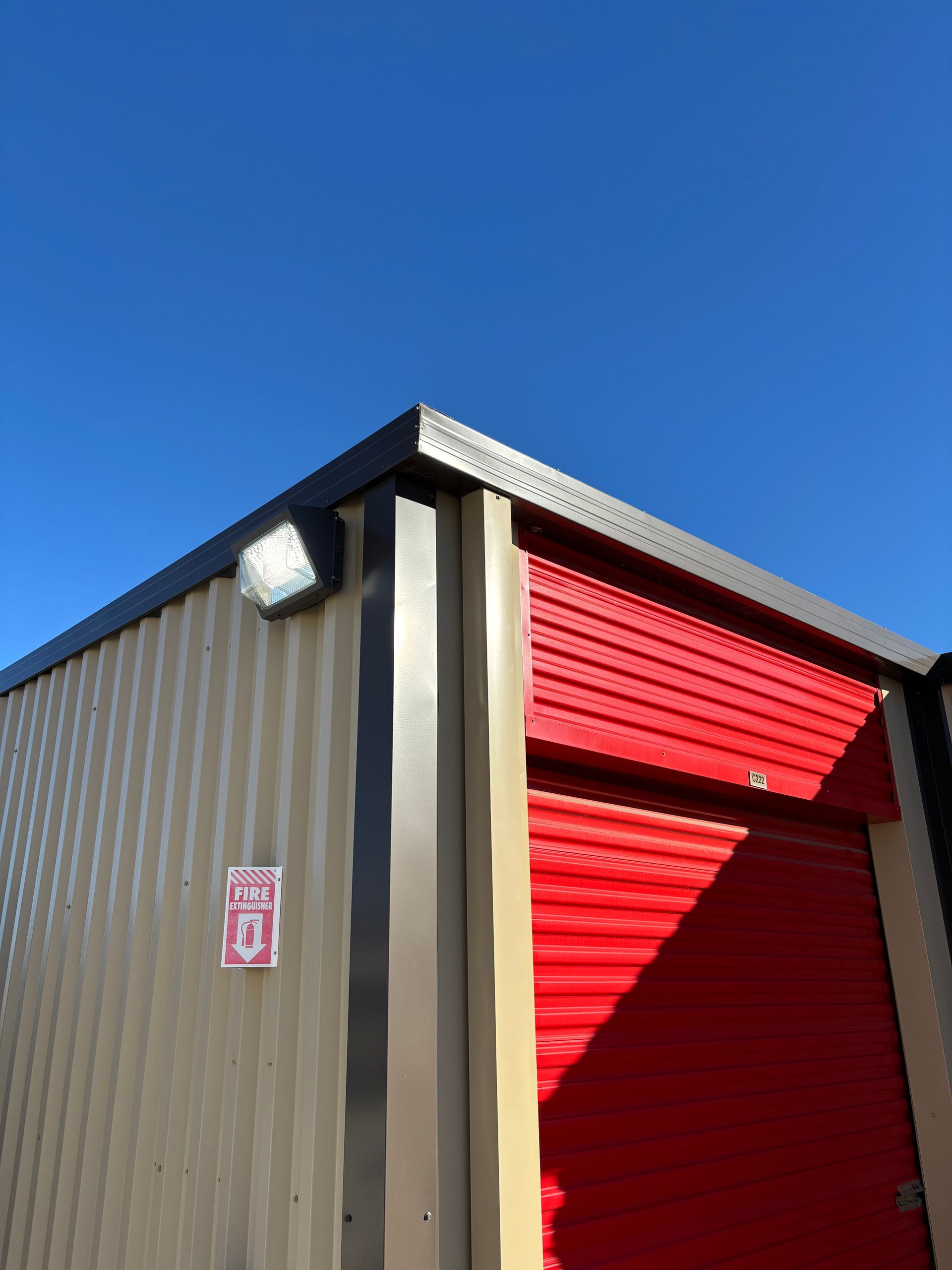 Storage unit building with a red door, tan siding, and bright blue sky.