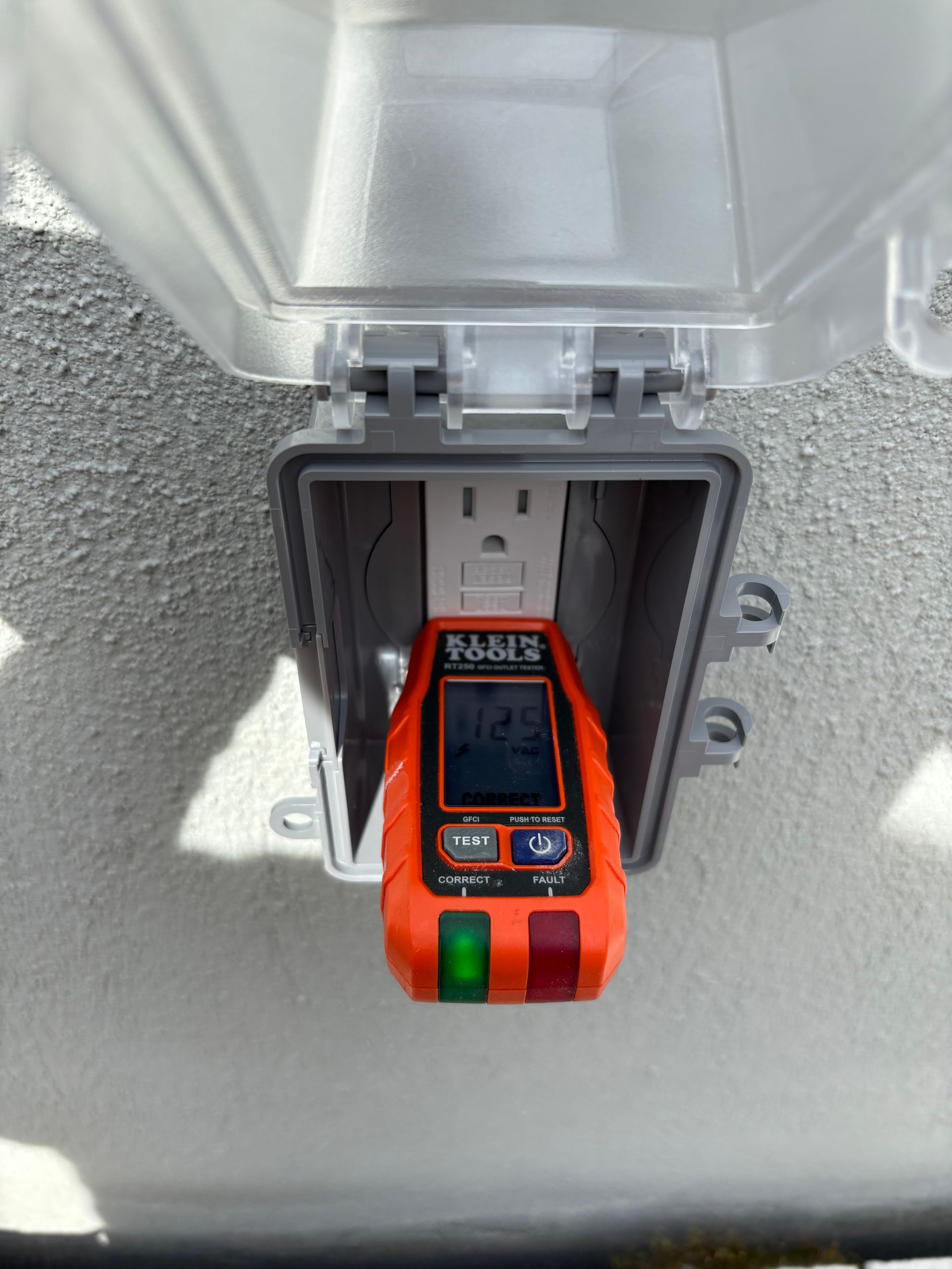 Orange electrical outlet tester plugged into outdoor outlet in a gray weatherproof box.