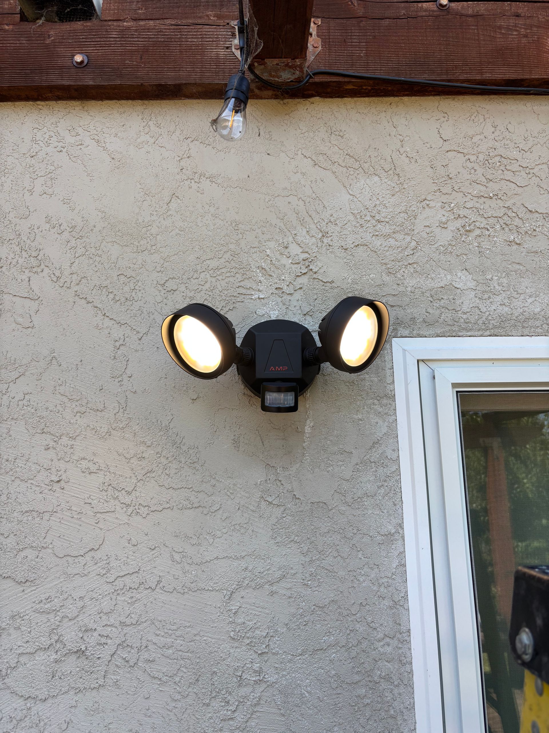 Motion-activated floodlights on a stucco wall, illuminating; a window frame is visible to the right.
