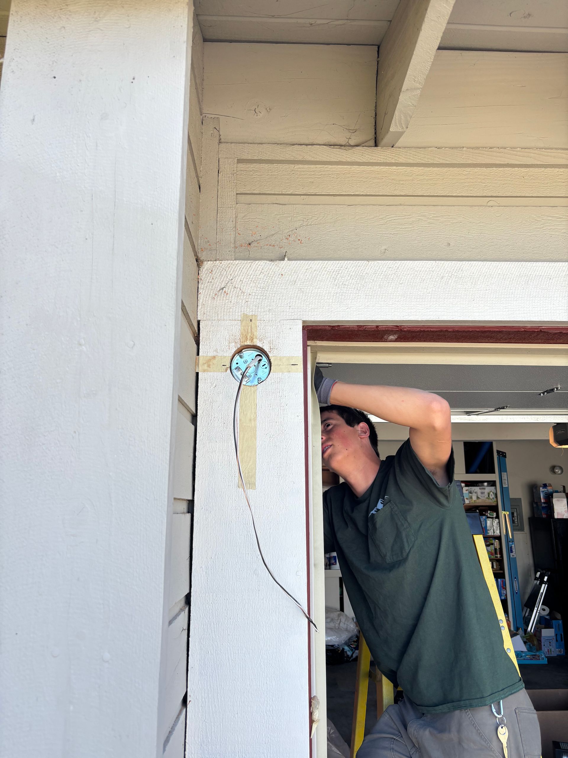 Man installs a small device on a door frame. White wall and tan trim are visible.