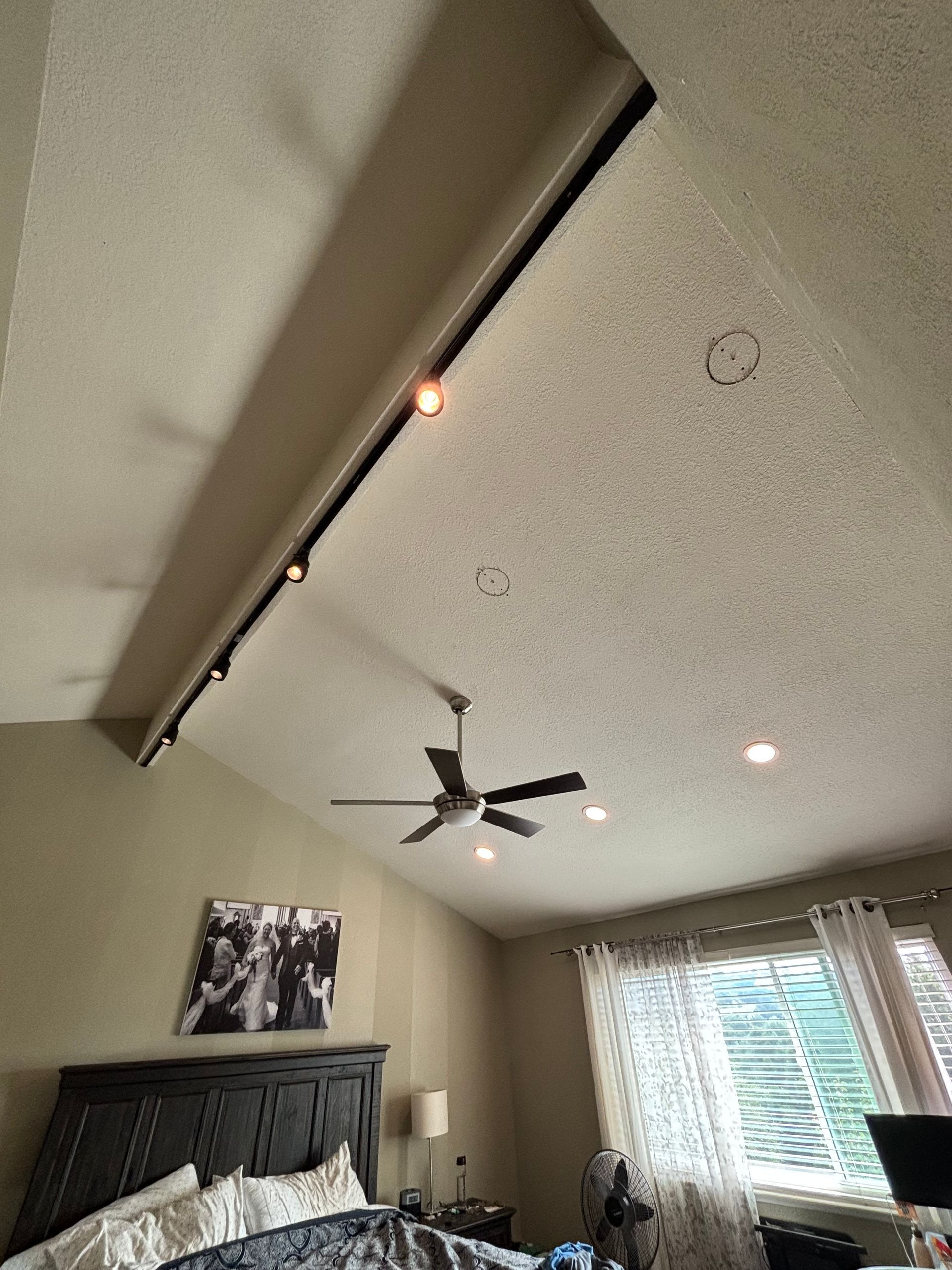 Bedroom ceiling with track lighting, ceiling fan, and bed.