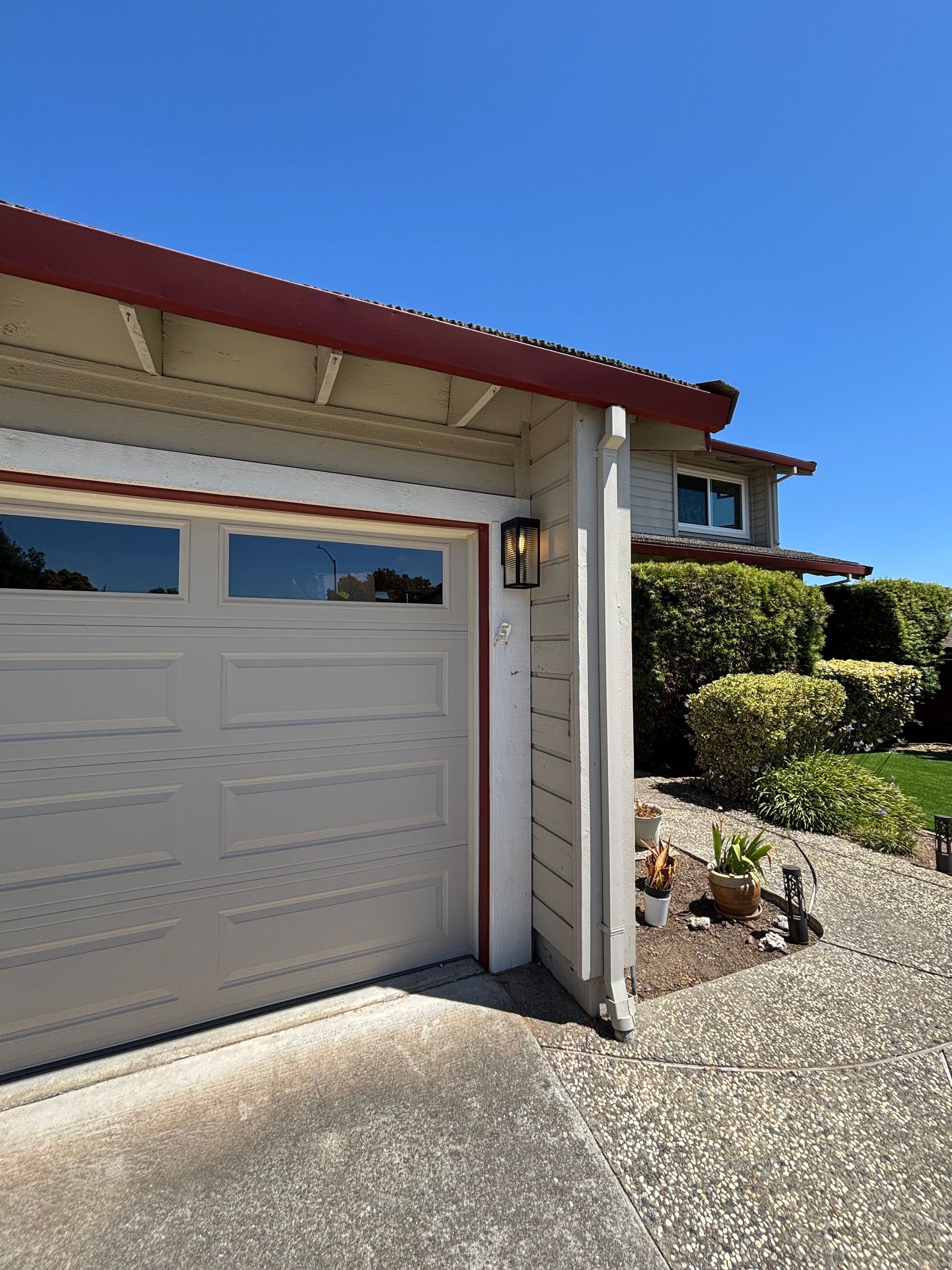 White garage door with windows, red trim, and a light fixture on a sunny day.