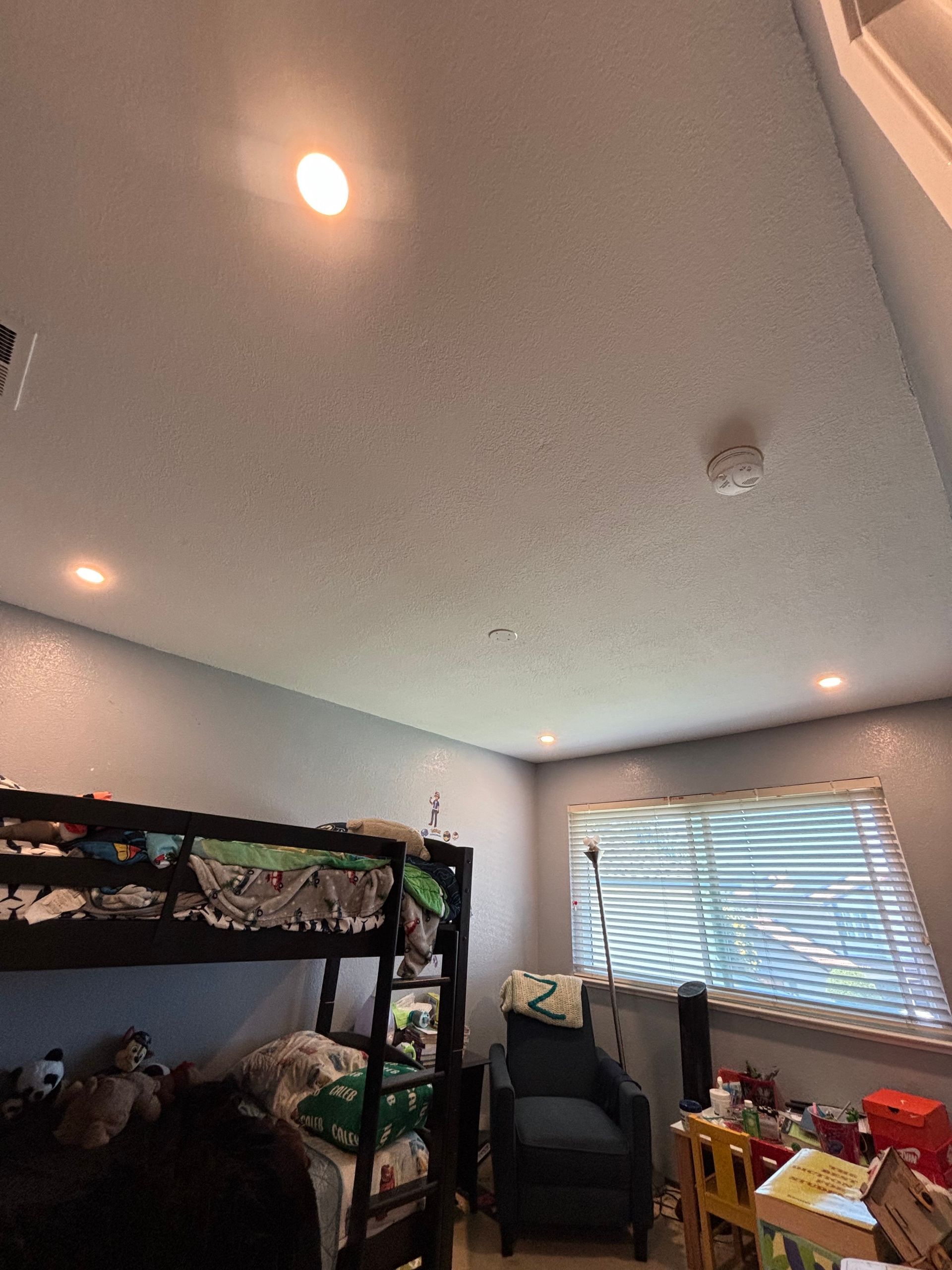 Bunk bed in a bedroom with a blue wall, blinds, and recessed ceiling lights.