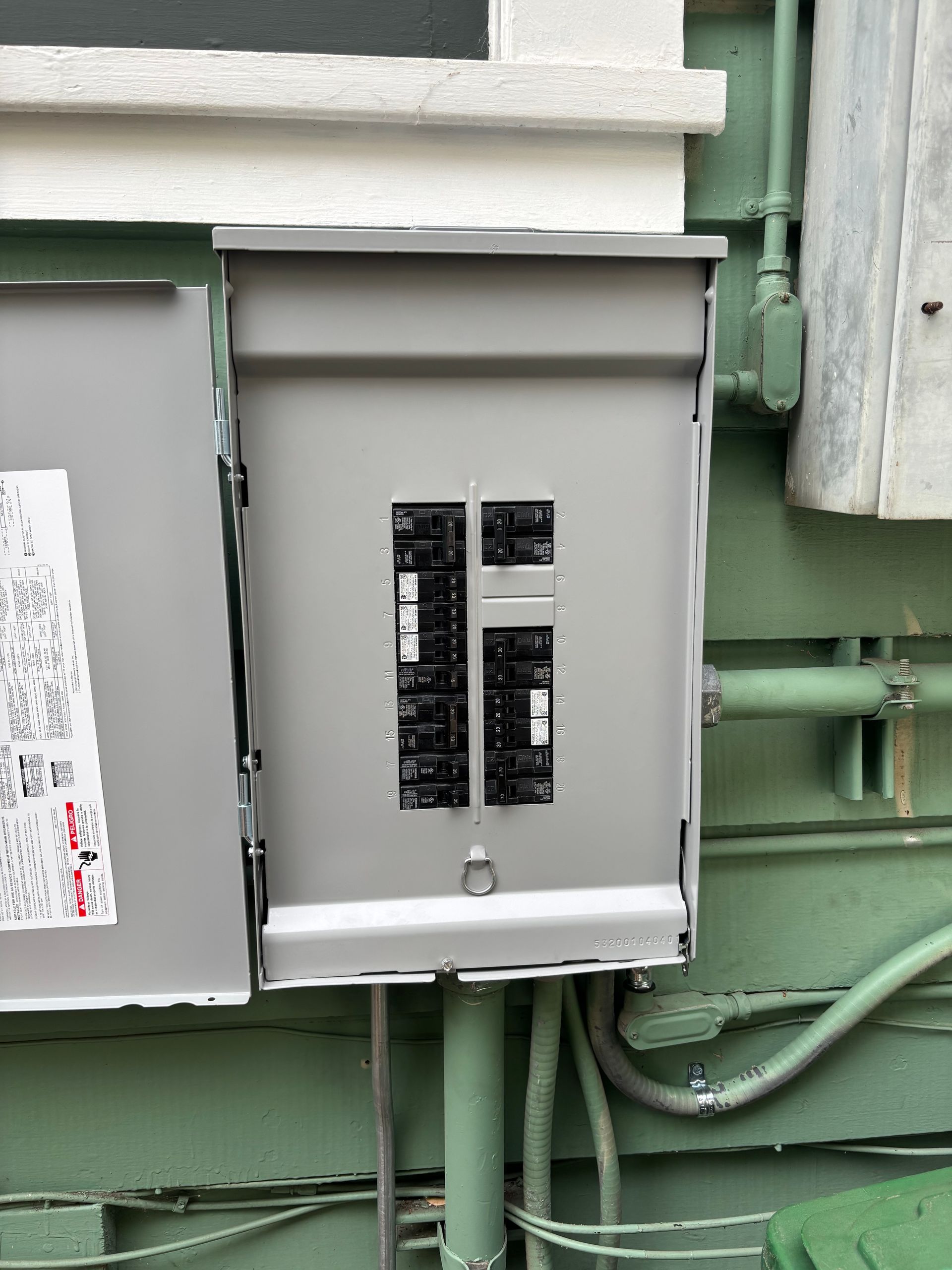 Electrical breaker box mounted on a green wall with a partially open door.