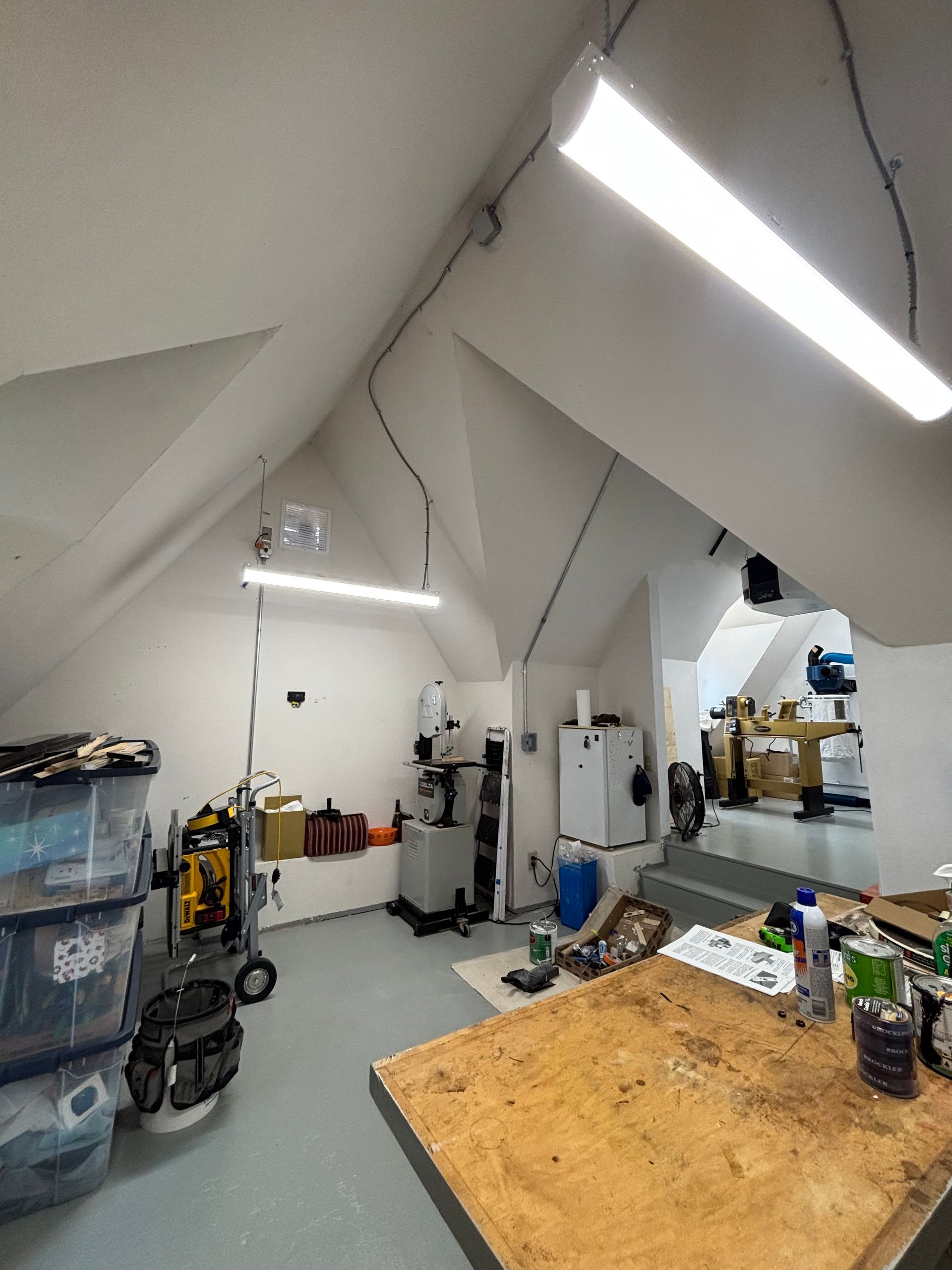 Workshop with workbench, tools, and machines in a bright, sloped-ceiling room.