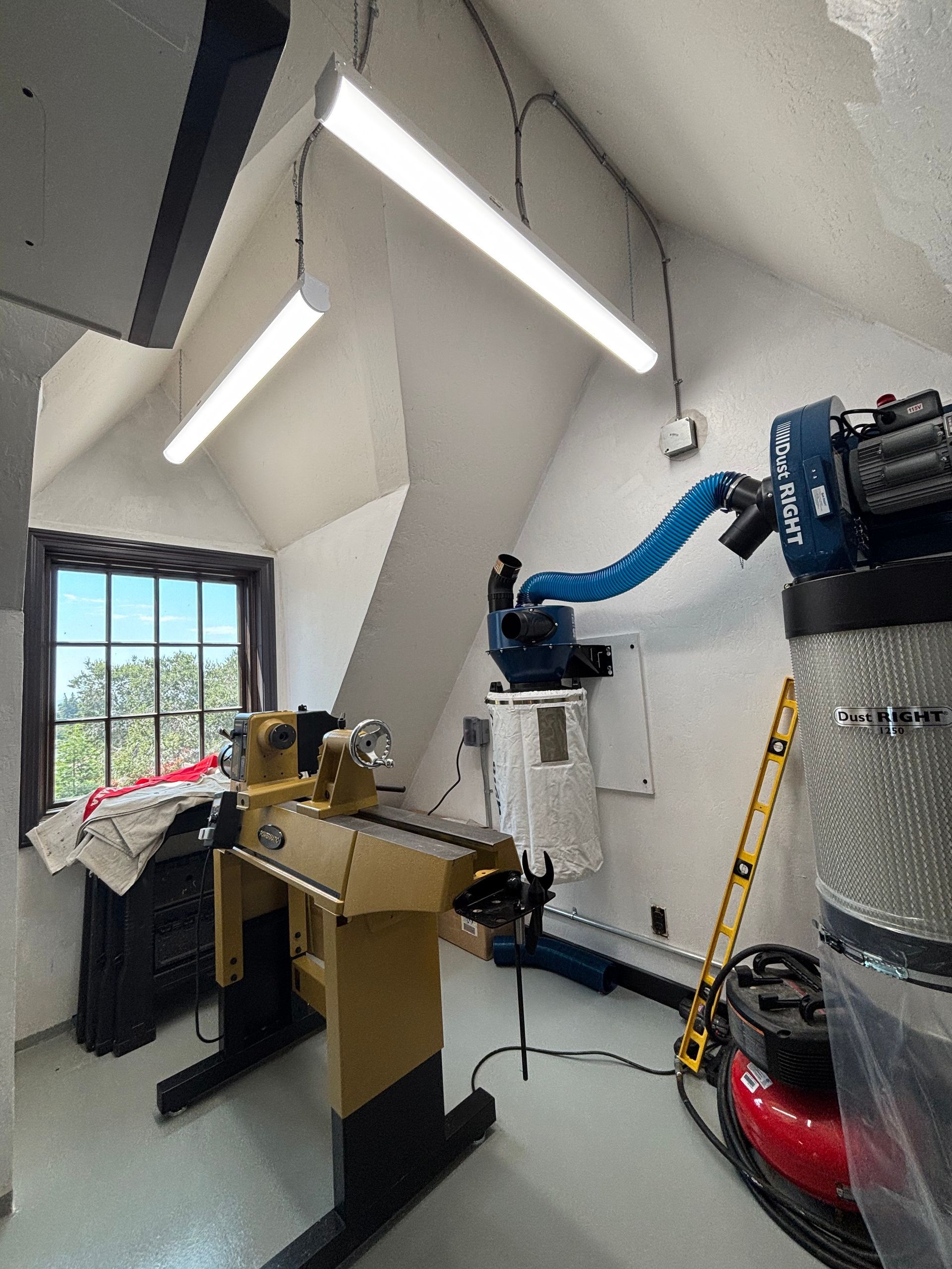 Workshop with wood lathe, dust collector, and fluorescent lights in a white-walled room.