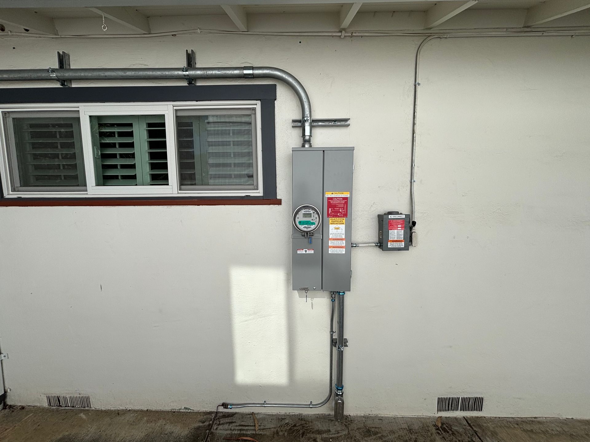 Electrical meter and panel mounted on a white wall, with conduit running along the wall.