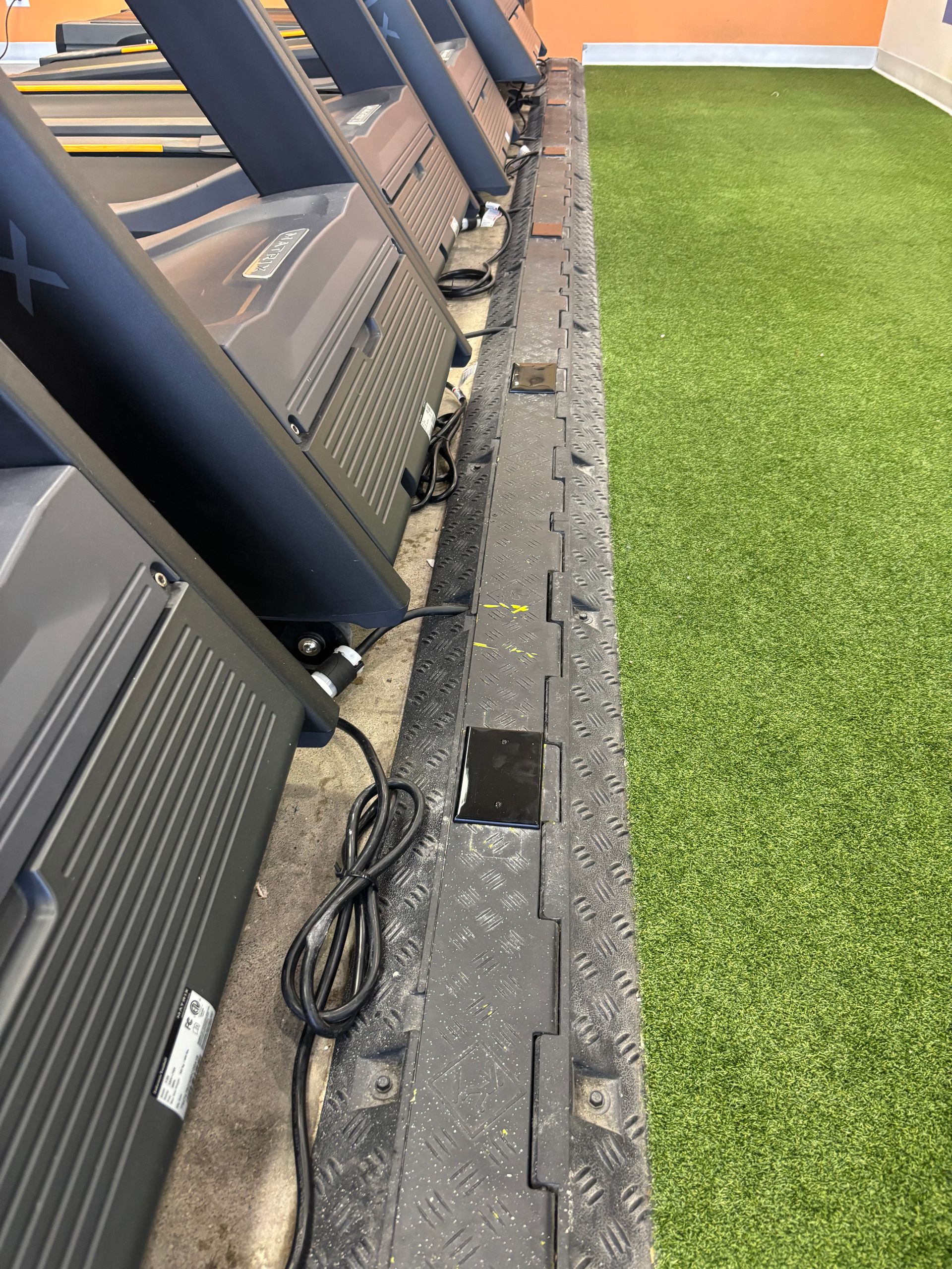 Row of treadmills in a gym setting next to artificial turf.