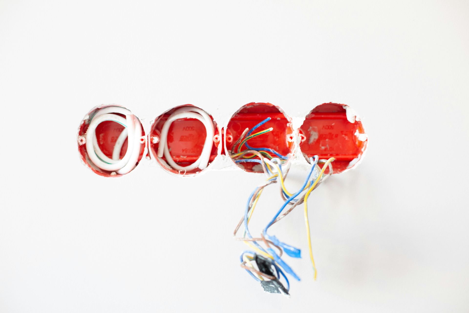Four red electrical boxes embedded in a white wall with exposed colored wires.