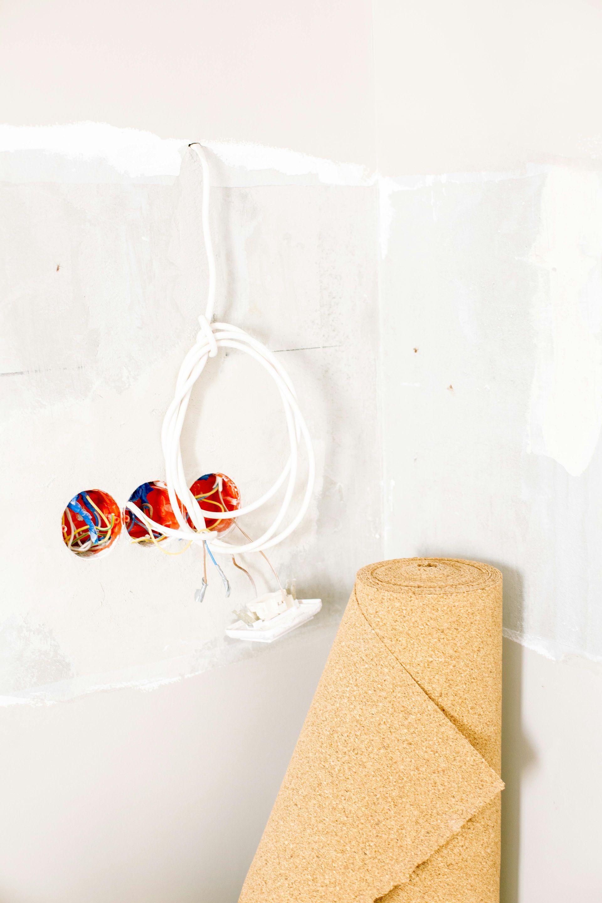 Electrical wiring and wall fixtures exposed during a renovation. A roll of tan cork material is nearby.