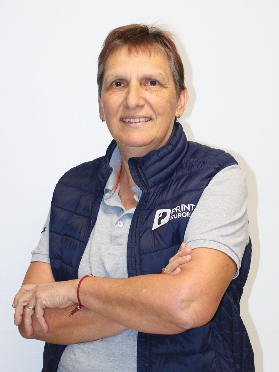 Une femme en chemise blanche est debout, les bras croisés et sourit.