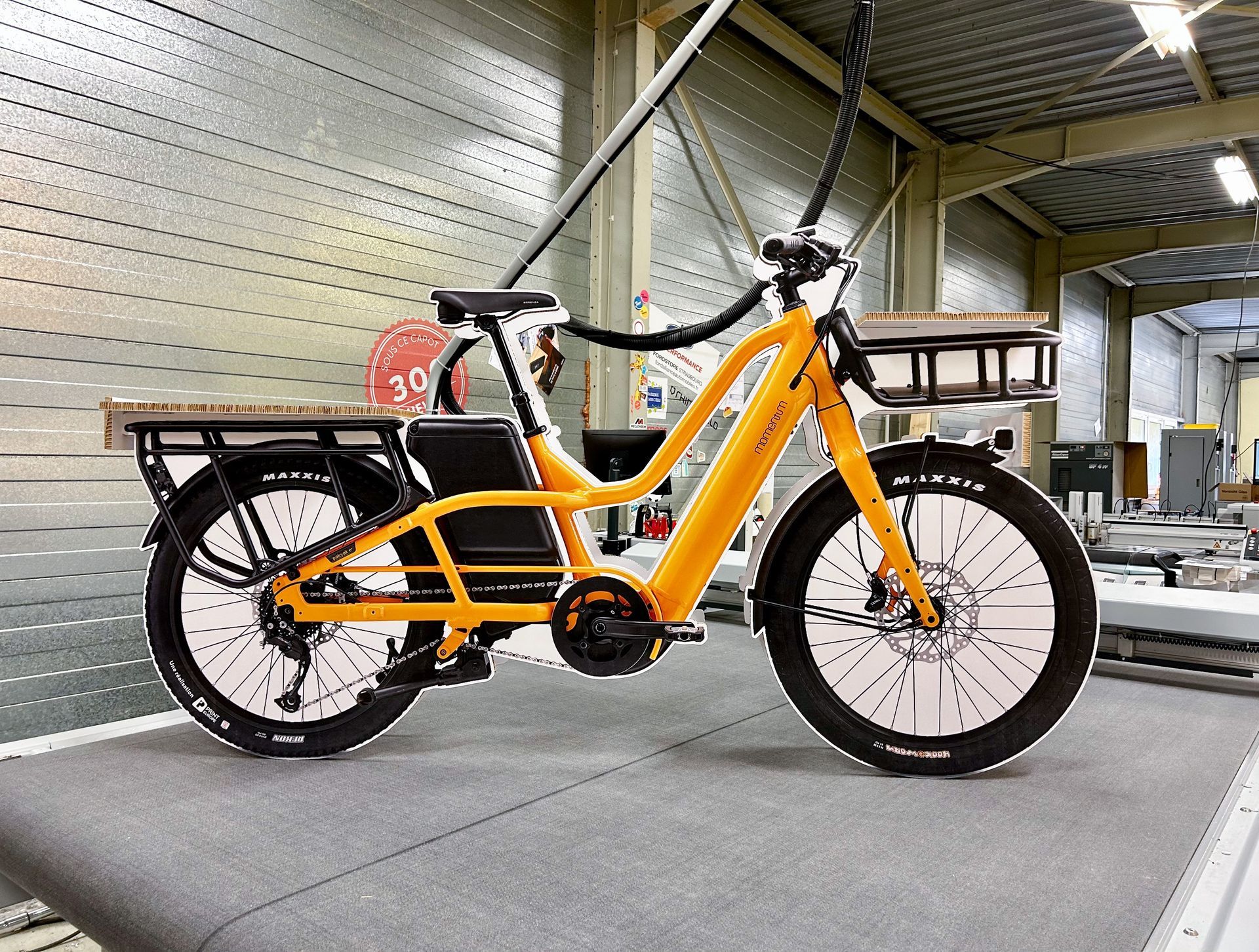 Un vélo jaune avec un panier à l'arrière est garé dans un entrepôt.