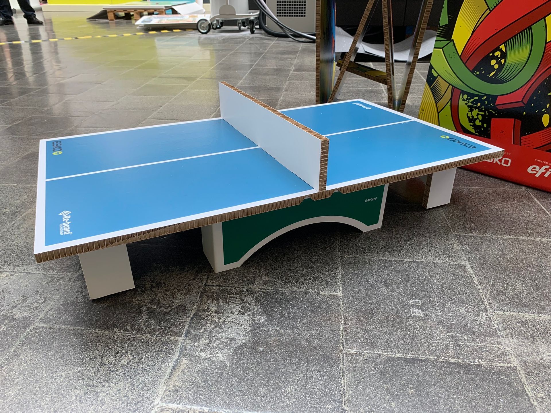 Une petite table de ping-pong est posée sur un sol carrelé.
