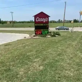 A Casey’s gas station sign stands in a grassy field, displaying fuel prices of 4.04 and 5.29, with a car in the background.