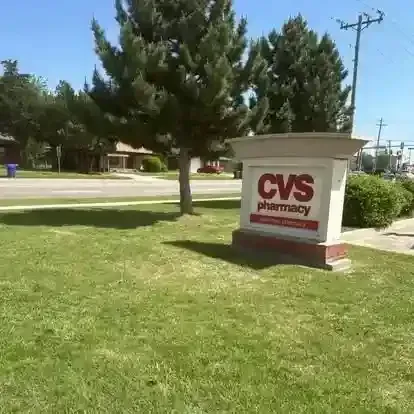 A CVS Pharmacy sign stands on a grassy lawn in front of a tree and road on a sunny day.