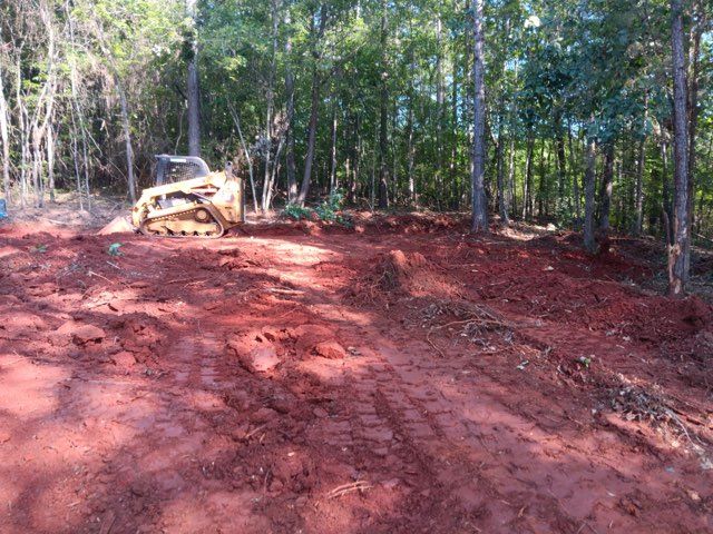 Bulldozer on a red dirt clearing in a wooded area.