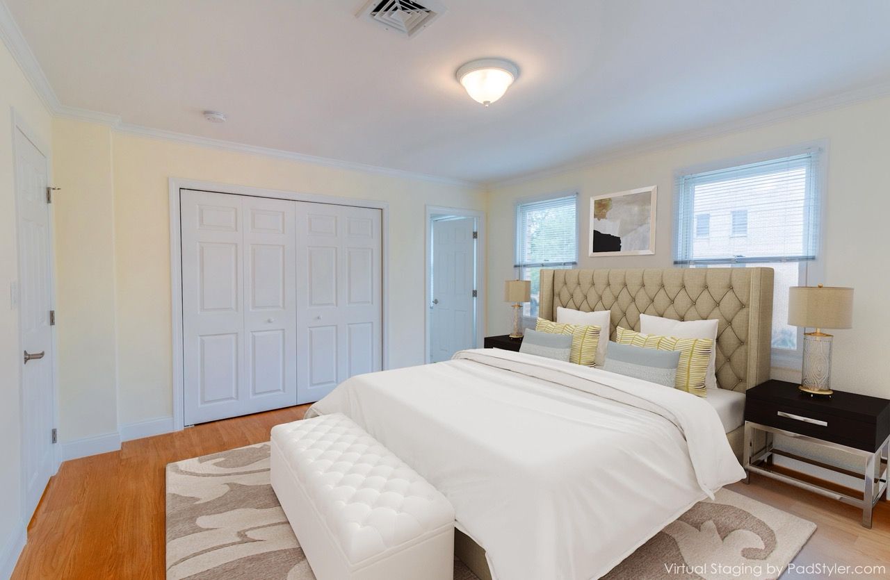 Bedroom in a modern apartment with a tufted beige headboard, white bedding, two nightstands, and a bench at the foot.