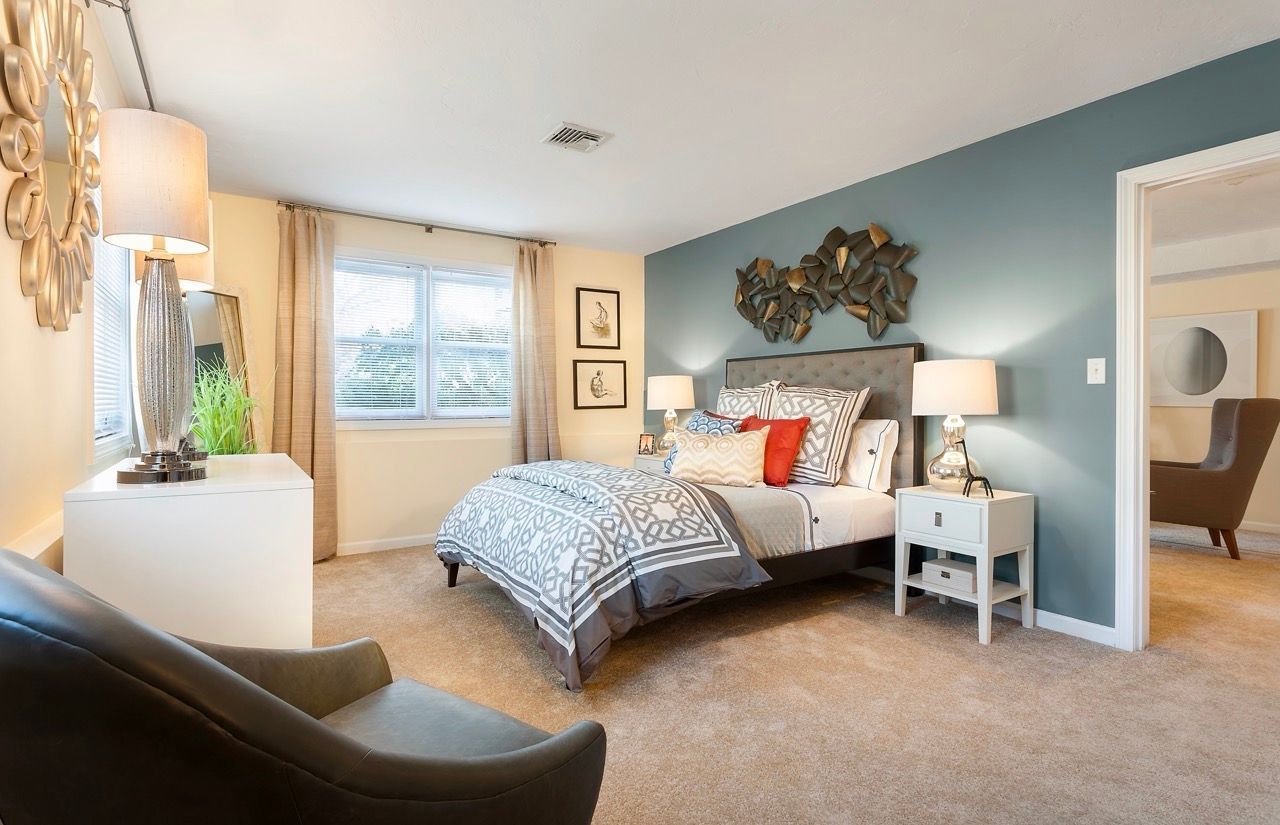 Bedroom in an apartment with a blue accent wall, bed, nightstands, and seating.