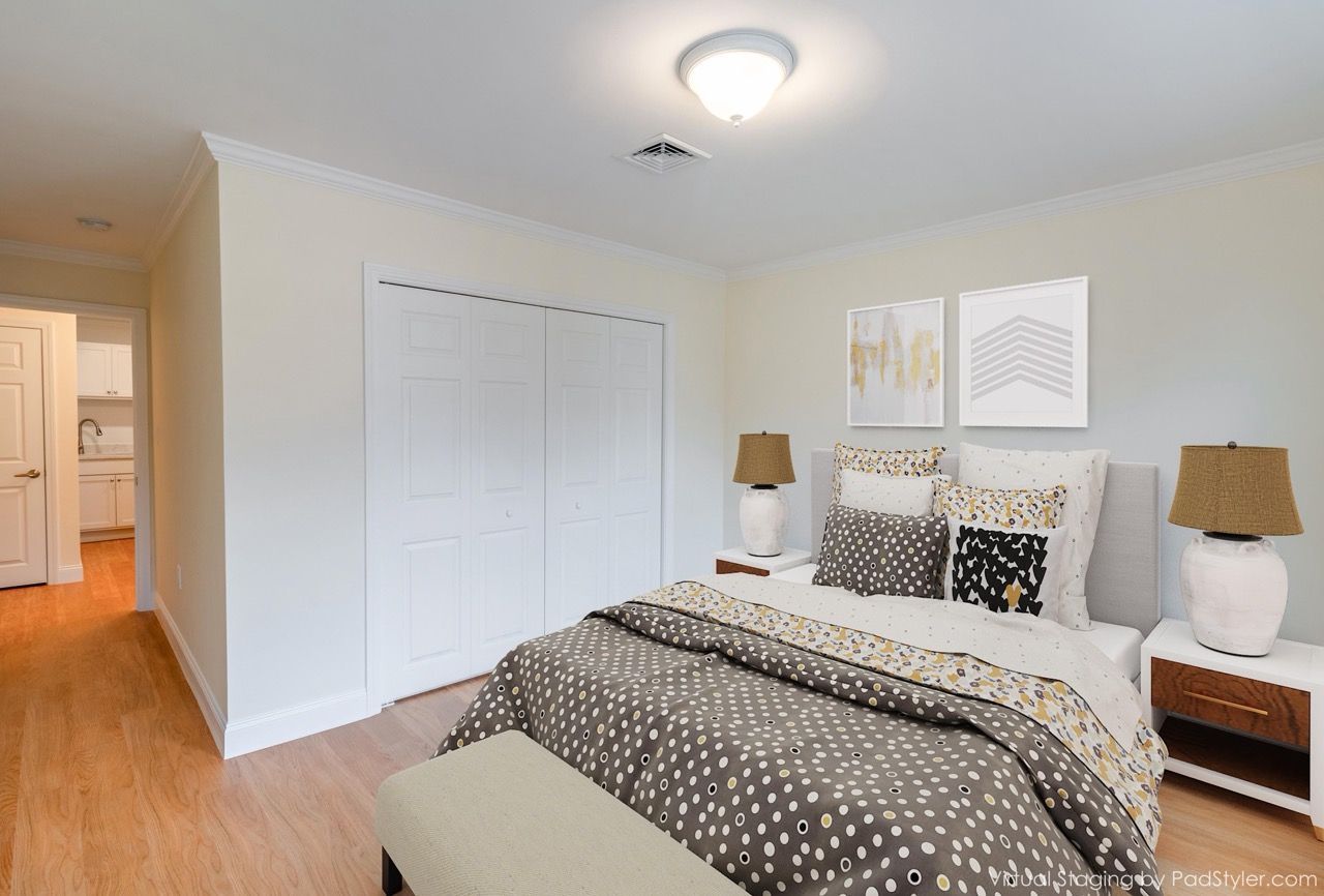 Bedroom with a neatly made bed, two white nightstands, matching lamps, and abstract art.