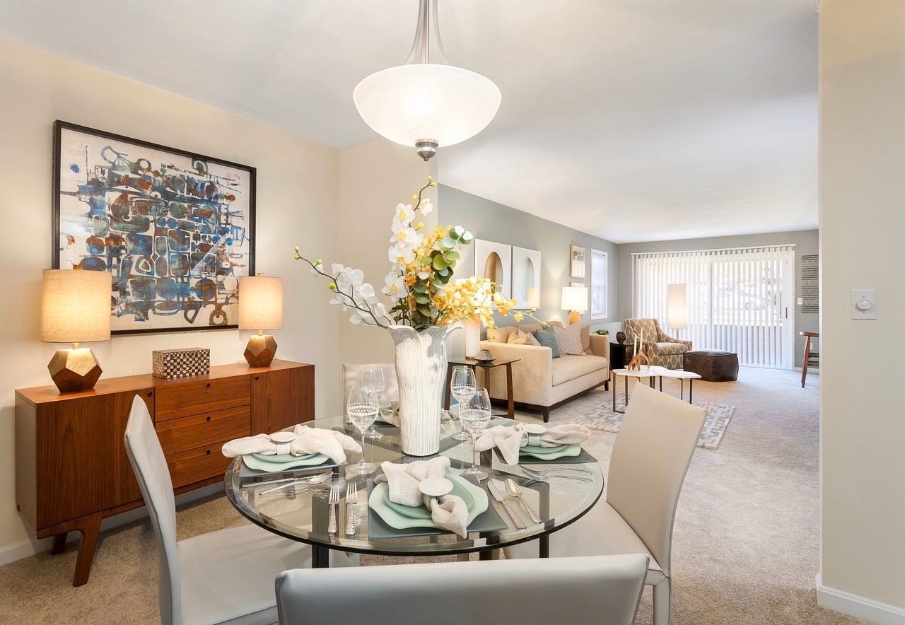 Open-plan dining and living area with a glass dining table, beige chairs, and neutral decor.