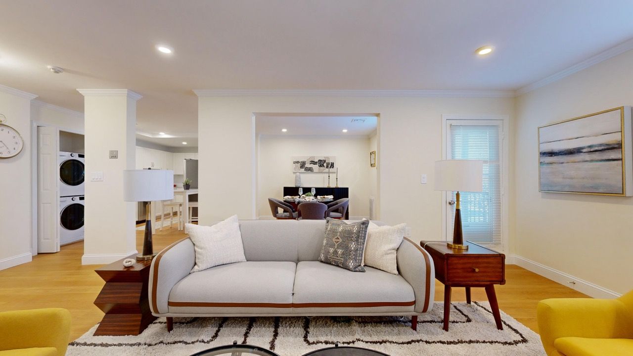 Bright living room with a light gray sofa, wooden end tables, and a view into the dining area.