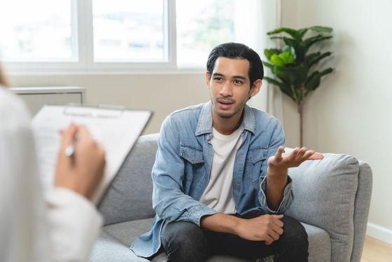 A man is sitting on a couch talking to a doctor.