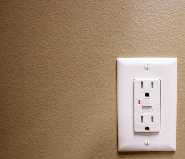 White electrical outlet with a red reset button on a tan wall.