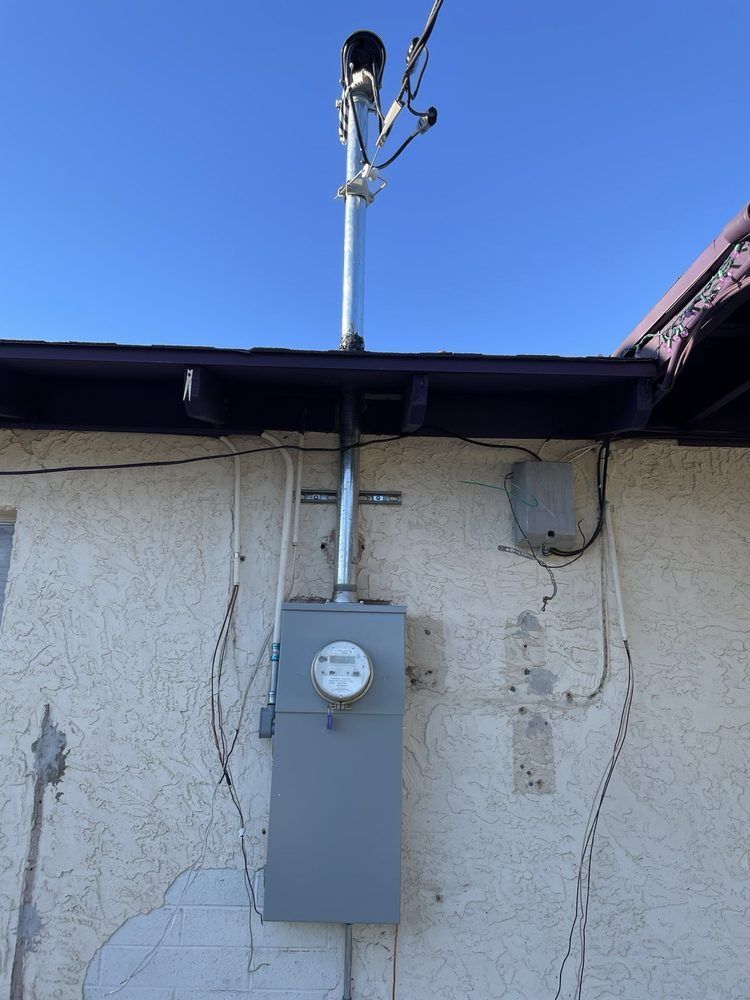 Electrical meter box and conduit on a stucco wall beneath a roofline.