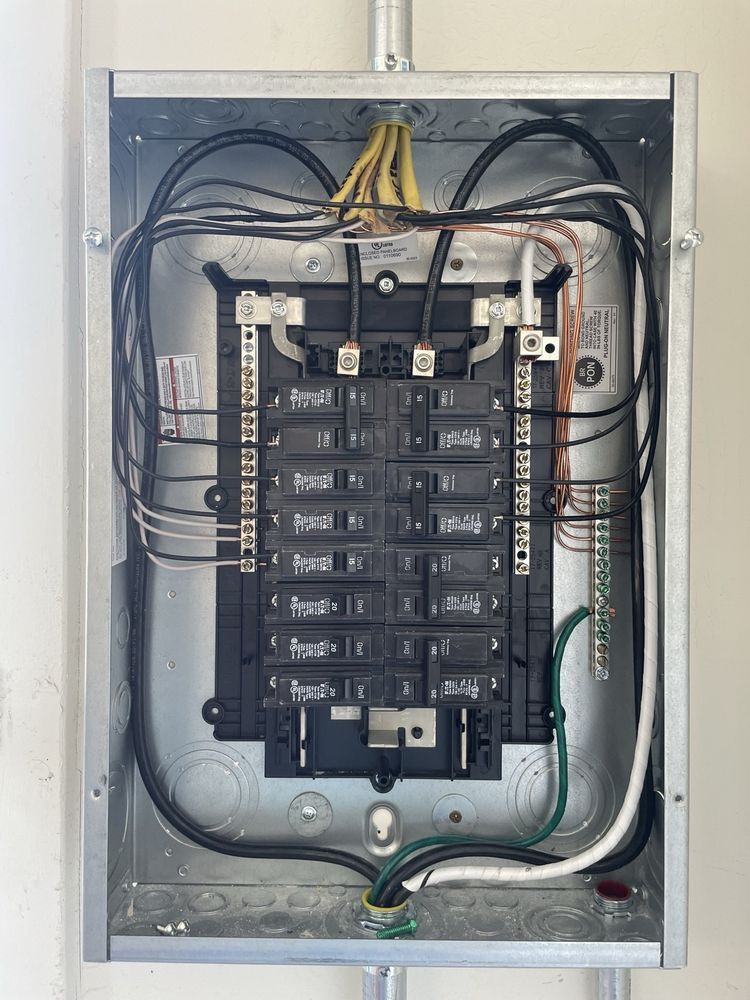 Electrical panel with wires and circuit breakers. Gray metal box mounted on a white wall.