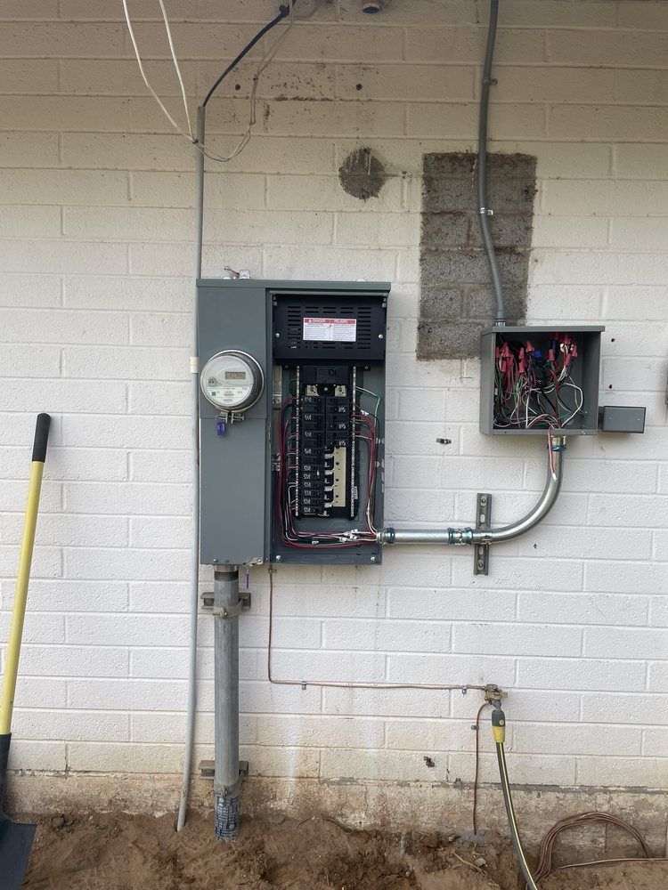 Electrical panel and meter mounted on a white brick wall. Conduit and wires visible.