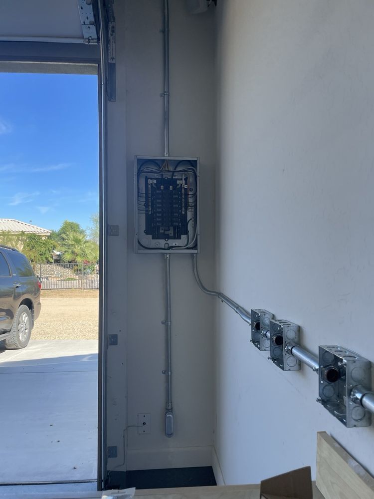 Electrical panel with conduit and junction boxes on a white wall. Garage door on left.