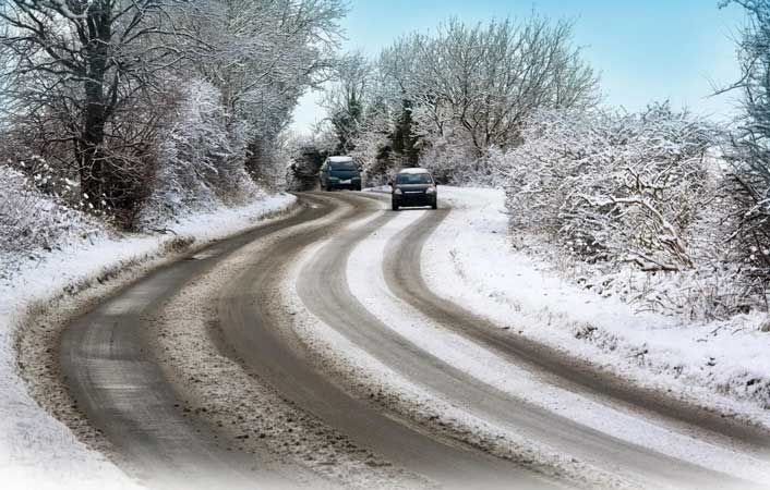 Two cars are driving down a snowy road.