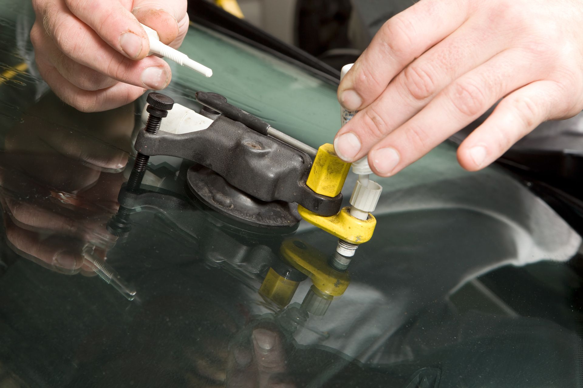 Close-up of a technician repairing a cracked windshield using specialized tools.