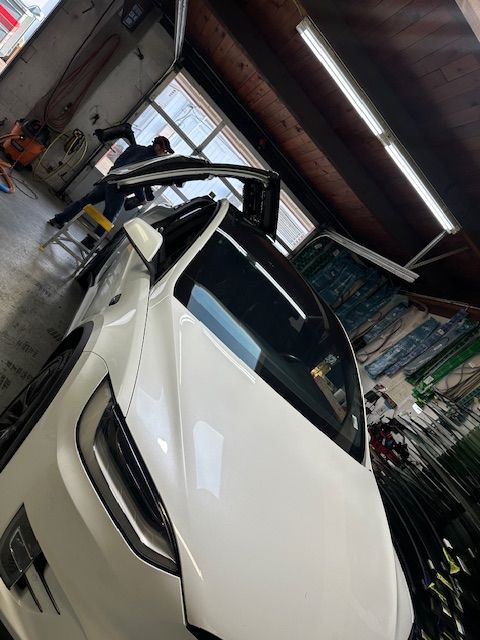 A white tesla model x is parked in a garage with its doors open.