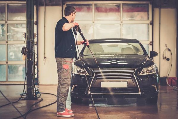 A man is washing a car with a high pressure washer in a garage.