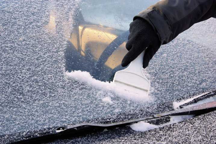 A person is cleaning the windshield of a car with a scraper.