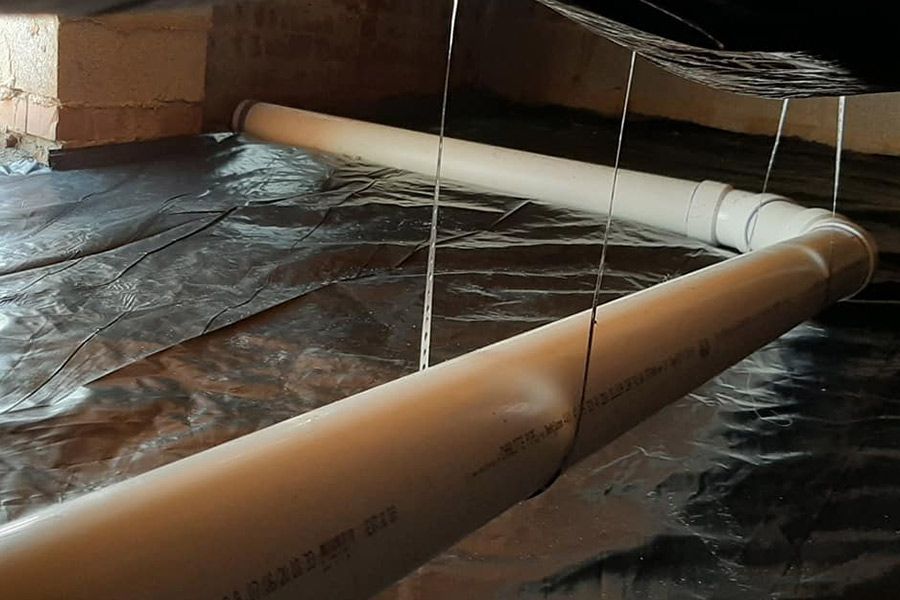 PVC pipes in crawl space, supported by wires, on reflective insulation layer.