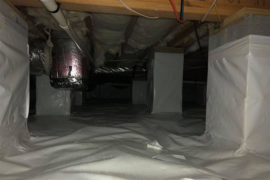 White plastic vapor barrier in a crawl space with support columns and ductwork.