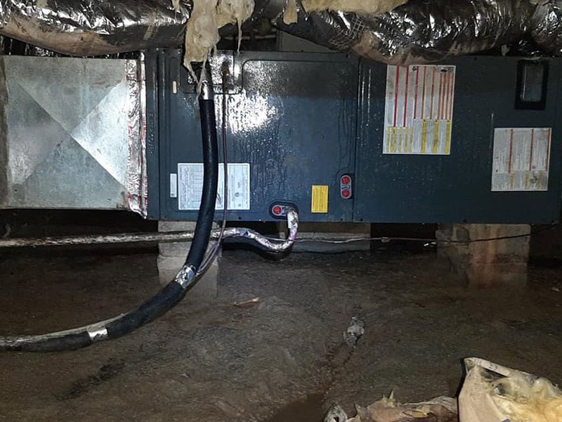 HVAC unit in a crawlspace with standing water. Ductwork and pipes are visible.