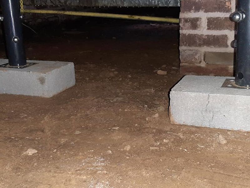 Two black poles secured to concrete blocks on a dirt floor; a brick wall is to the right.